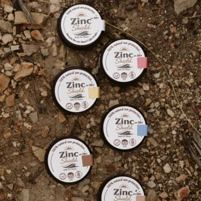 ZincShield SPF 50 mineral sunscreen tins in multiple colours on rocky ground.