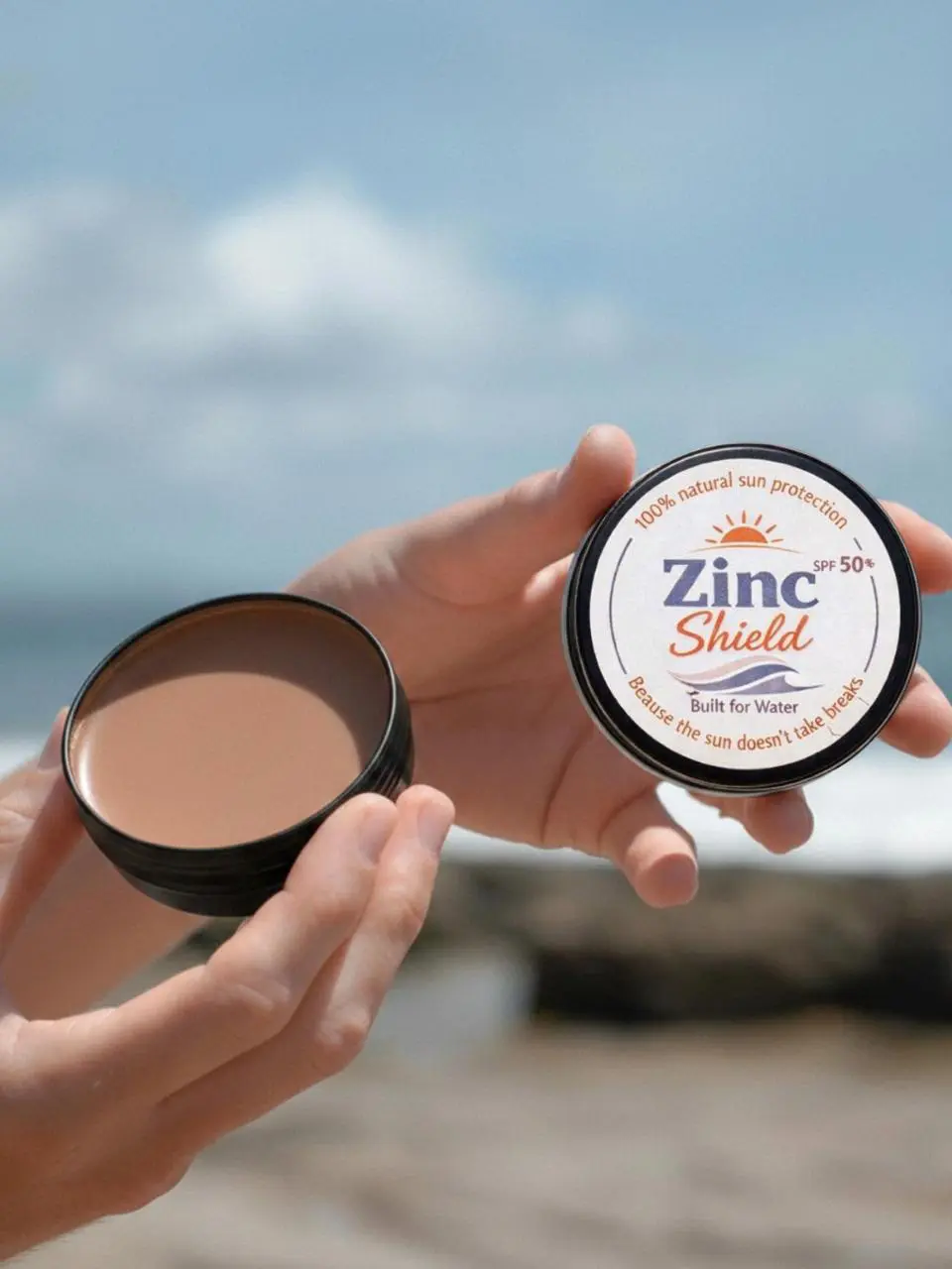 Hands holding open Zinc Shield natural mineral zinc sunscreen tin - creamy texture and easy application