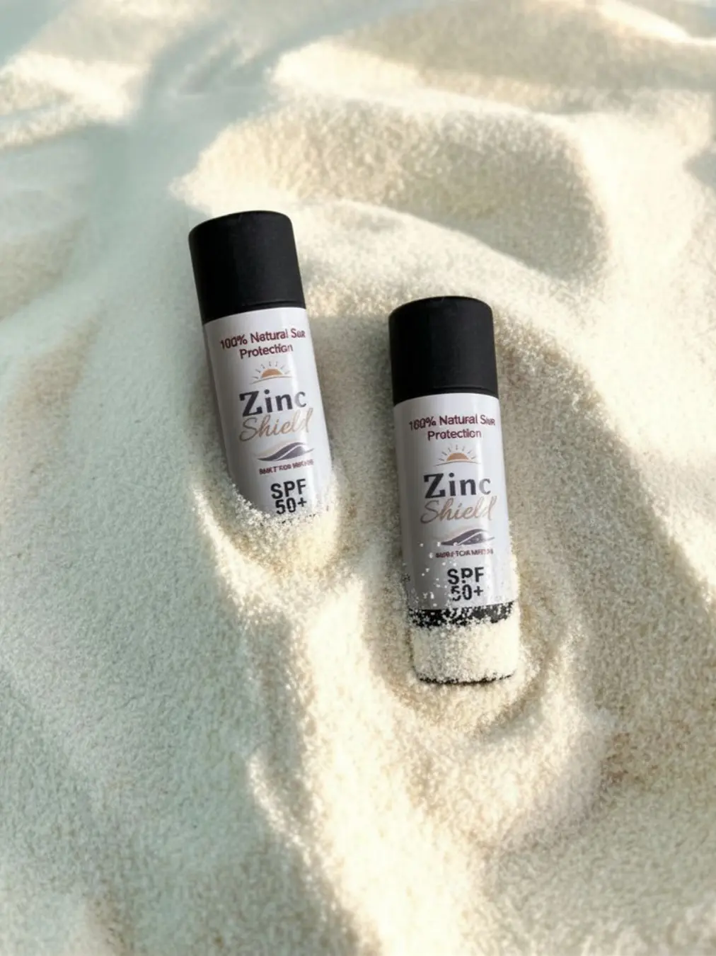 Two Zinc Shield natural zinc sunscreen bottles standing in beach sand - 100% mineral formula