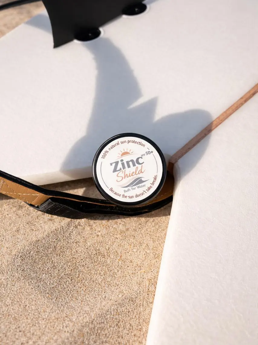 Zinc Shield natural mineral sunscreen tin resting on surfboard at the beach - reef safe sun protection