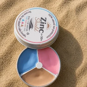 ZincShield SPF 50 tinted zinc sunscreen palette displayed on beach sand.